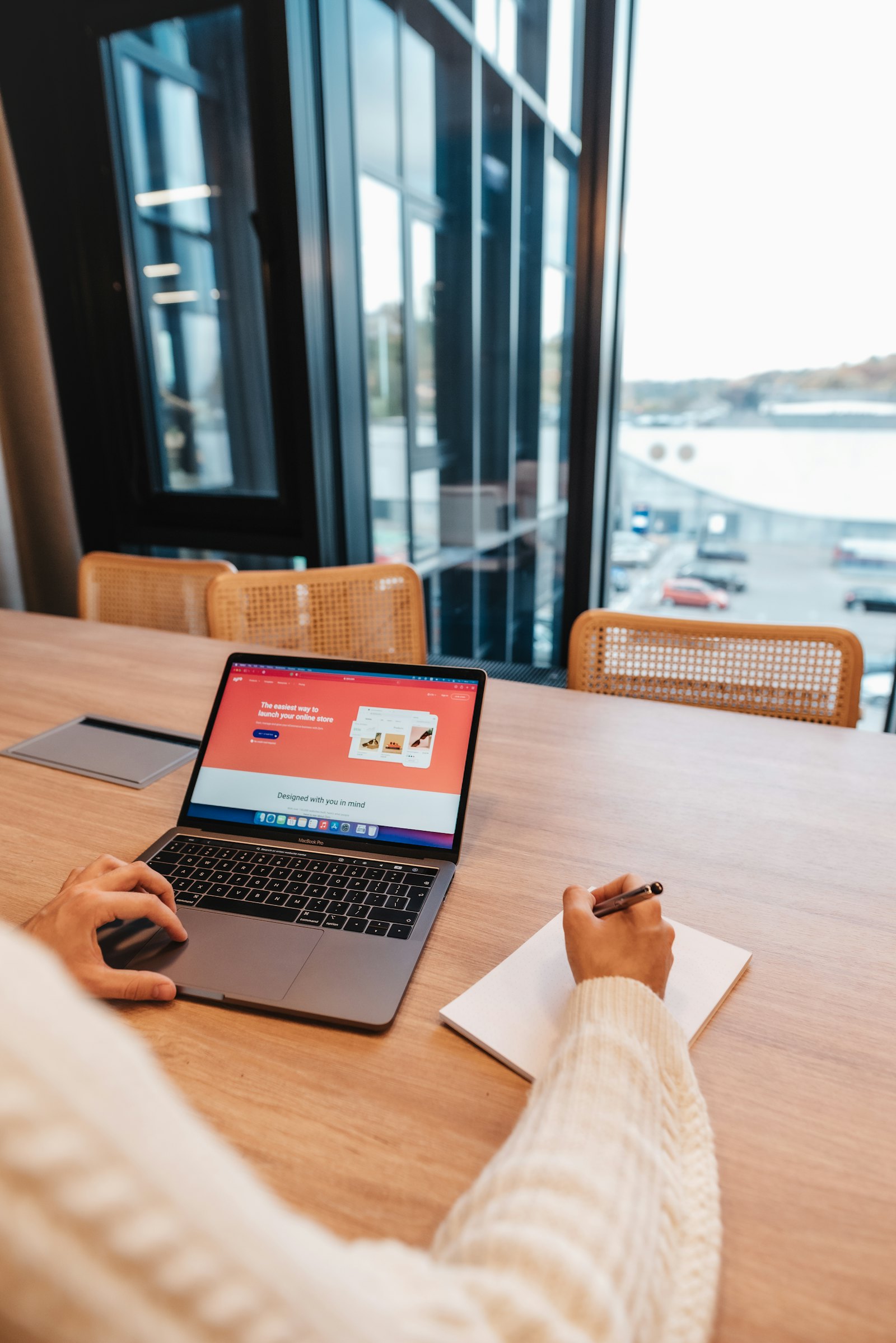 Aan een bureau bij het raam werkt iemand aan een nieuwe website op een laptop