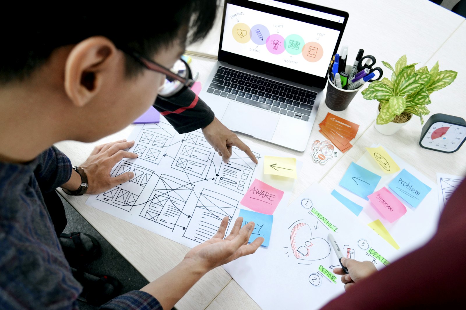 Webdesigner werkt aan wireframes en de planning van een website naast een laptop